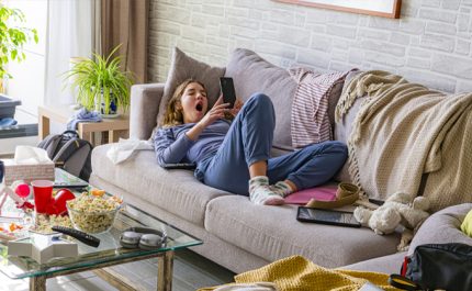 ベッドの上で寝っ転がってスマホを操作するスウェット姿の女性