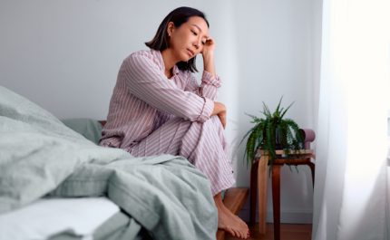 ベッドの上で膝をかかえ、頬杖をついて悩む女性